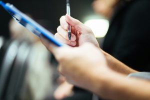 a hand holds a pen, which hovers above a clipboard