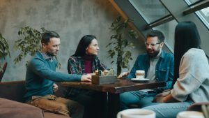 a man speaks to the others gathered around a small table, while they listen attentively